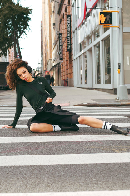 Woman in a Lemmi label green athletic top and tennis skirt sitting on a crosswalk in an urban setting