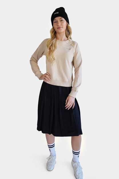 Lemii Label - Woman wearing a black ribbed knit hat, beige crew sweater, short athletic black skirt and white crew socks- white background. 