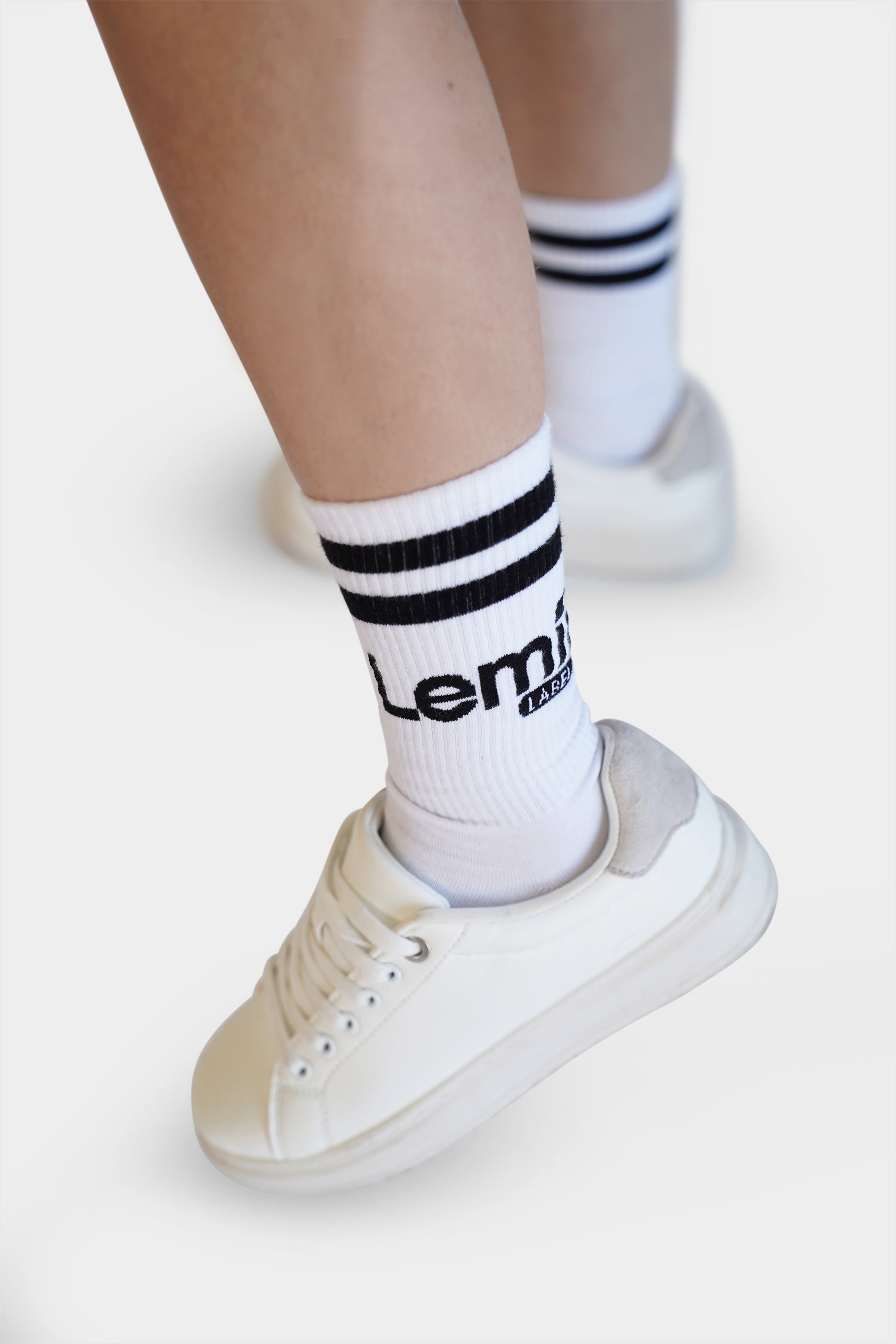 Lemii Label - White sneakers with black stripes worn on a plain background