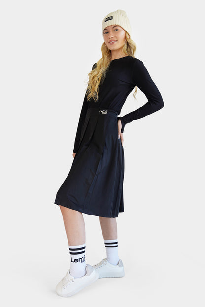 Lemii Label - Woman wearing a black athletic pleated skirt and top, white sneakers, and a cream beanie on a white background