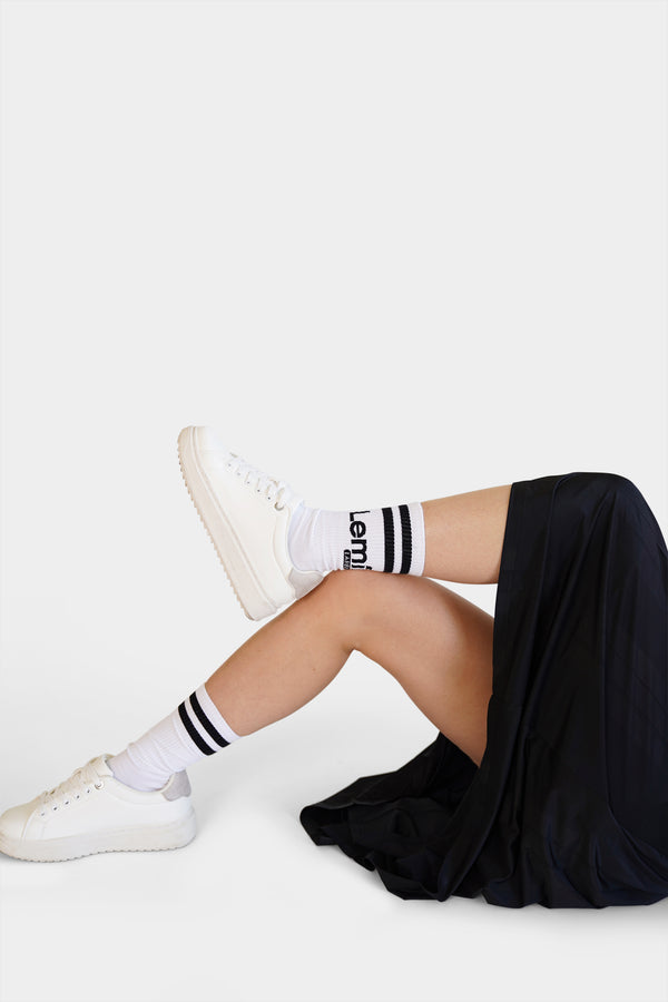 Lemii Label  - Person wearing white sneakers and black and white striped socks with a black skirt on a light White -background