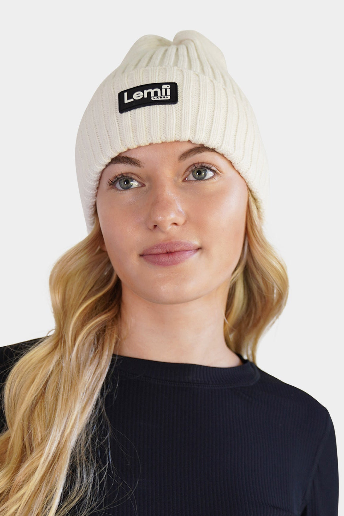 Lemii Label -Woman wearing a black athletic long-sleeve shirt and white beanie with a brand logo on a white background
