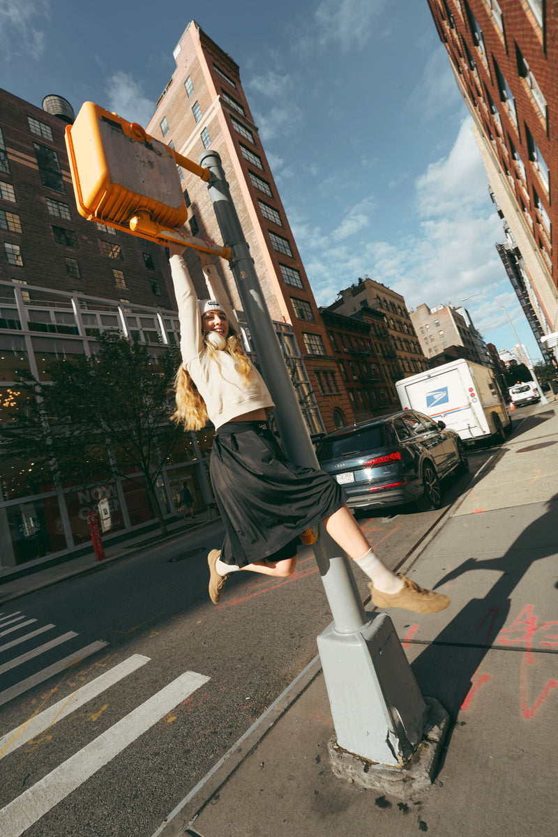 Lemii Label - Woman hanging from street sign in the city wearing athletic clothing.