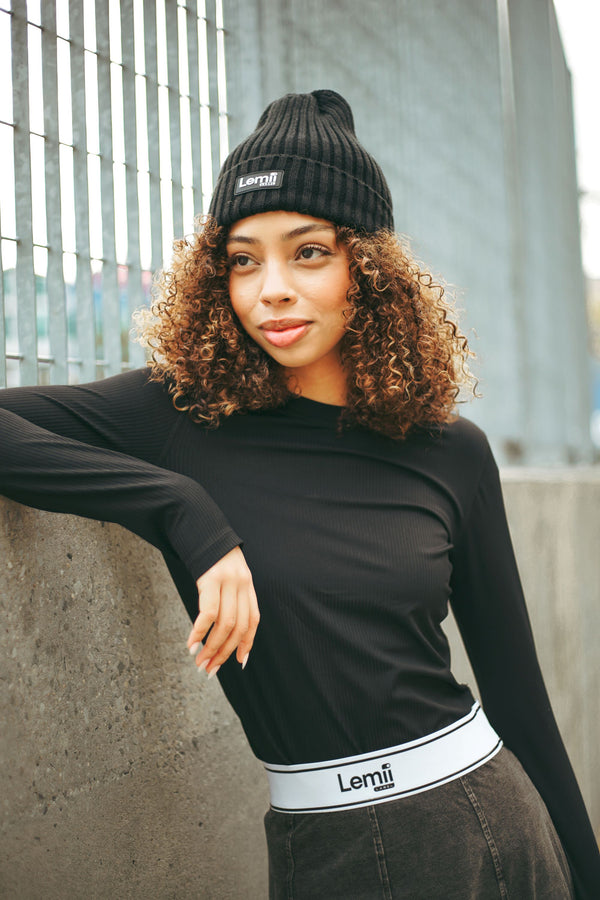 Person wearing a black beanie and black long-sleeve shirt with Lemii Label Logo - leaning against a concrete wall.